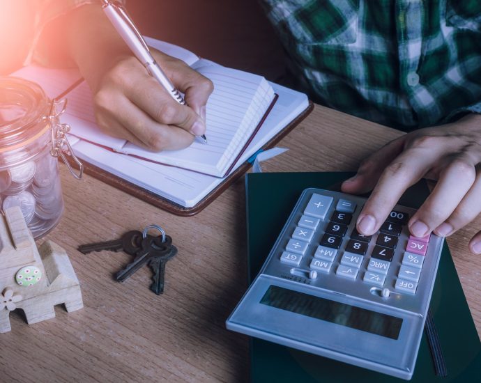 Person calculating financial data with a calculator and notebook, symbolizing automated loan processing using LLM orchestration and retrieval-augmented generation.