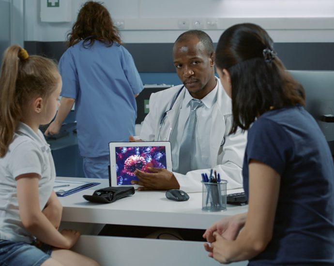 Doctor explaining medical data insights to a parent and child using a tablet, showcasing HIPAA-compliant predictive analytics in a clinical setting.
