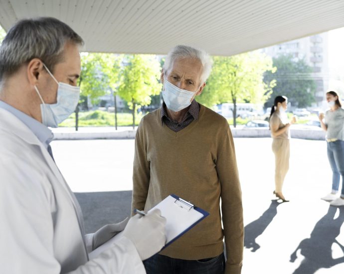 Doctor recording patient information on a clipboard during check-in, illustrating predictive analytics streamlining patient intake and appointment scheduling.