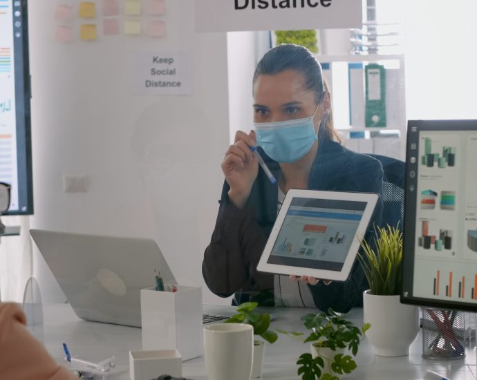 Healthcare professional reviewing patient data on a tablet with analytics dashboards, representing AI-driven scheduling optimization and reduced patient access delays.