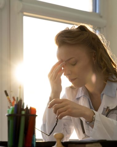 Exhausted doctor experiencing documentation fatigue while working on a computer in a clinical setting.