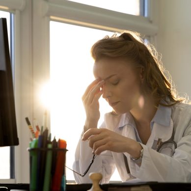 Exhausted doctor experiencing documentation fatigue while working on a computer in a clinical setting.