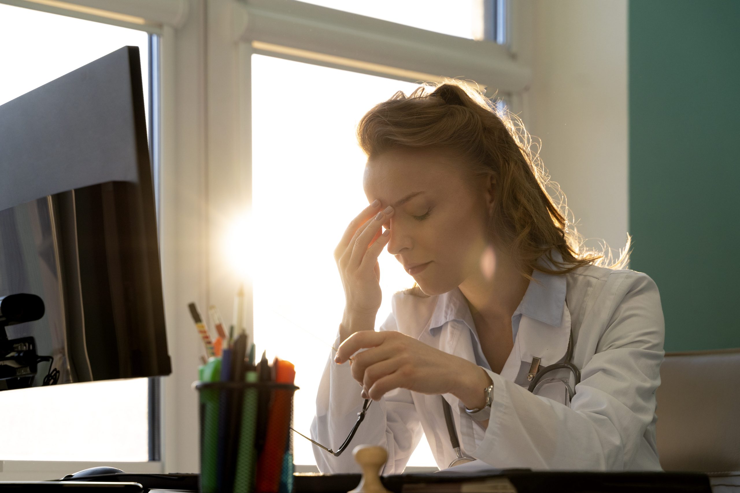 Exhausted doctor experiencing documentation fatigue while working on a computer in a clinical setting.