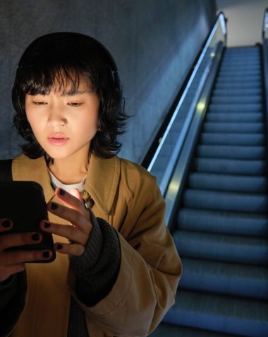 Urban lifestyle and people. Woman in headphones, looks serious at her smartphone app, checking map, public transport schedule with worried face, standing on escalator