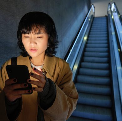 Urban lifestyle and people. Woman in headphones, looks serious at her smartphone app, checking map, public transport schedule with worried face, standing on escalator