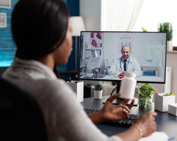 Patient having a virtual consultation with a doctor via video call on a desktop computer, discussing medication during an online healthcare session.